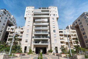 A multi-story residential building with balconies, a central entrance, and surrounding greenery.