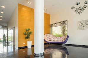 Un hall d’entrée moderne avec une grande colonne, une plante en pot, un fauteuil coloré et une fenêtre avec des stores.