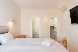 A hotel room with a bed, a nightstand, a TV mounted on the wall, and a bathroom visible through an open door. - Mamad Urban Gem • Outdoor Lounge by SeaNRent (Tel Aviv-Yafo)
