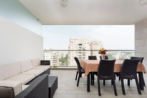 A balcony with a sofa and dining table, overlooking a cityscape.