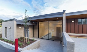 A modern building with a glass entrance, a staircase, and a small garden area with plants.