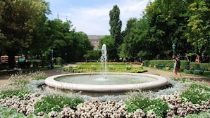 A park with a circular fountain surrounded by flower beds and trees. - Budapest Passage 1 (Budapest)