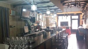 Una zona de bar con una barra alargada, múltiples luces colgantes y suelo de baldosas.