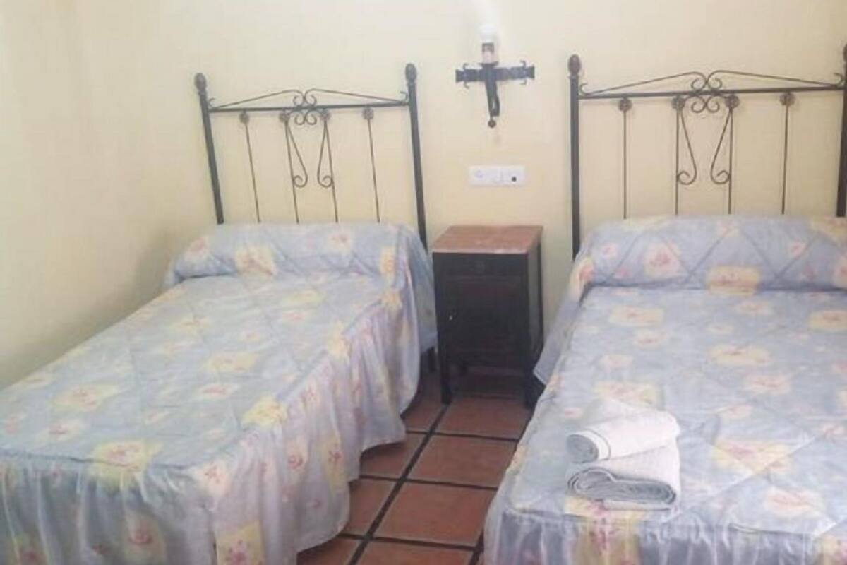 A small, clean room with two single beds, a nightstand, and a wall-mounted light fixture.
