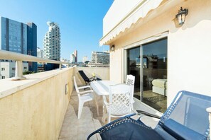 Un balcone con tavolo e sedie, una porta scorrevole in vetro che dà su una stanza e vista sulla città.