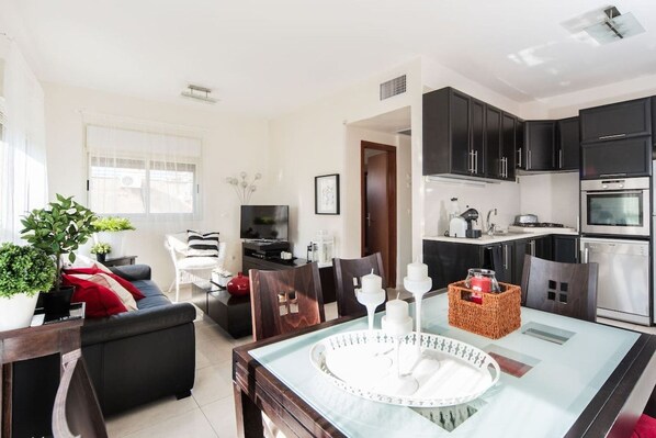 A modern living room with a sofa, a dining table, and a kitchen area with dark cabinets and appliances.