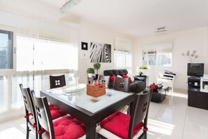 A modern living room with a glass dining table, red cushions, a black sofa, and a television.