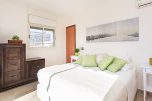 A bedroom with a bed, dresser, window, and a cityscape painting.