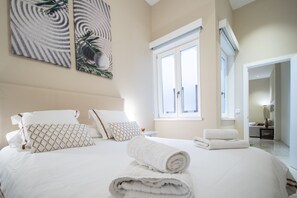 Una habitación de hotel con cama, almohadas, una toalla enrollada y obras de arte en la pared.