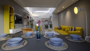 A modern living room with a dining table set for six, a yellow sofa, and a kitchen in the background. - BNB Medina (Marrakech)