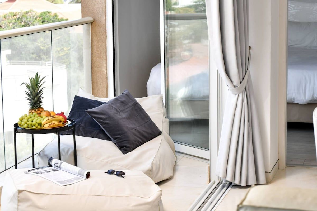 A balcony with a seating area, a small table with fruits, and a bed with a curtain.