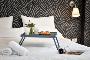 Una cama bien hecha con ropa blanca, una bandeja con croissants y una taza, y una pared con estampado de cebra.