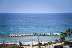 Vista costera con un rompeolas rocoso, playa y un mar azul cristalino.
