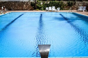 Una piscina con agua cristalina, rodeada de sillones blancos y un muro de piedra.