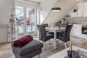 Eine moderne Küche mit weißen Schränken, einem Esstisch und Stühlen. Ein rotes Handtuch liegt auf einer Bank, und eine Champagnerflasche steht auf dem Tisch.