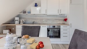 Moderni keittiö, jossa on valkoiset kaapit, marmoripintainen välitila ja ruokailutila, jossa on aamupalalle katettu pöytä.