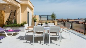 Una terraza en la azotea con una mesa, sillas, una escalera y vistas de la ciudad.