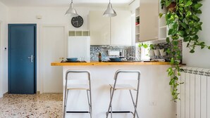 Una cocina con salpicadero de azulejos, un reloj, dos taburetes de bar y una puerta azul.