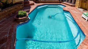A rectangular swimming pool with a blue edge, surrounded by red tiles.