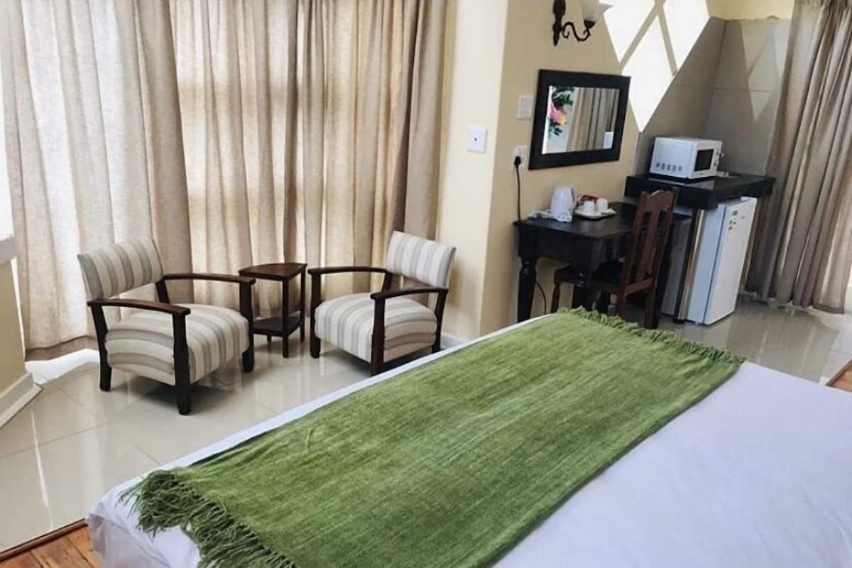 Habitación de hotel con una cama, un plaid verde, dos sillones, una mesita y un escritorio con una computadora y un microondas.
