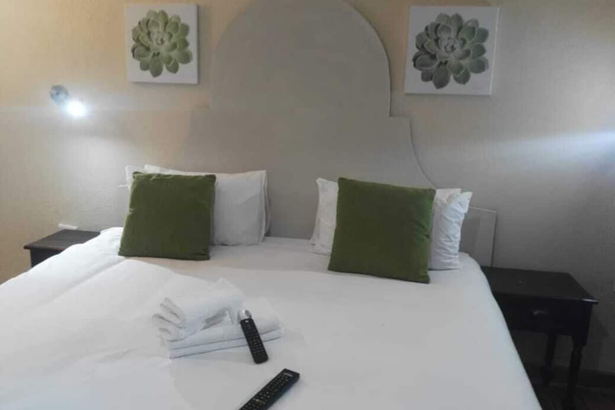 Una cama bien hecha con sábanas blancas, almohadas verdes, un control remoto y una toalla doblada sobre la cama.