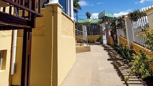 A reception area with a sign, a gated entrance, and a pathway leading to a building with a yellow facade.