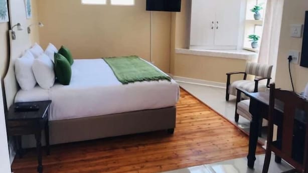 A bedroom with a bed, a desk, a chair, a TV, and a window.