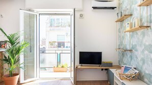 Un saló modern amb una porta corredissa de vidre, un televisor de pantalla plana, una planta en test i una estant mural amb objectes decoratius.
