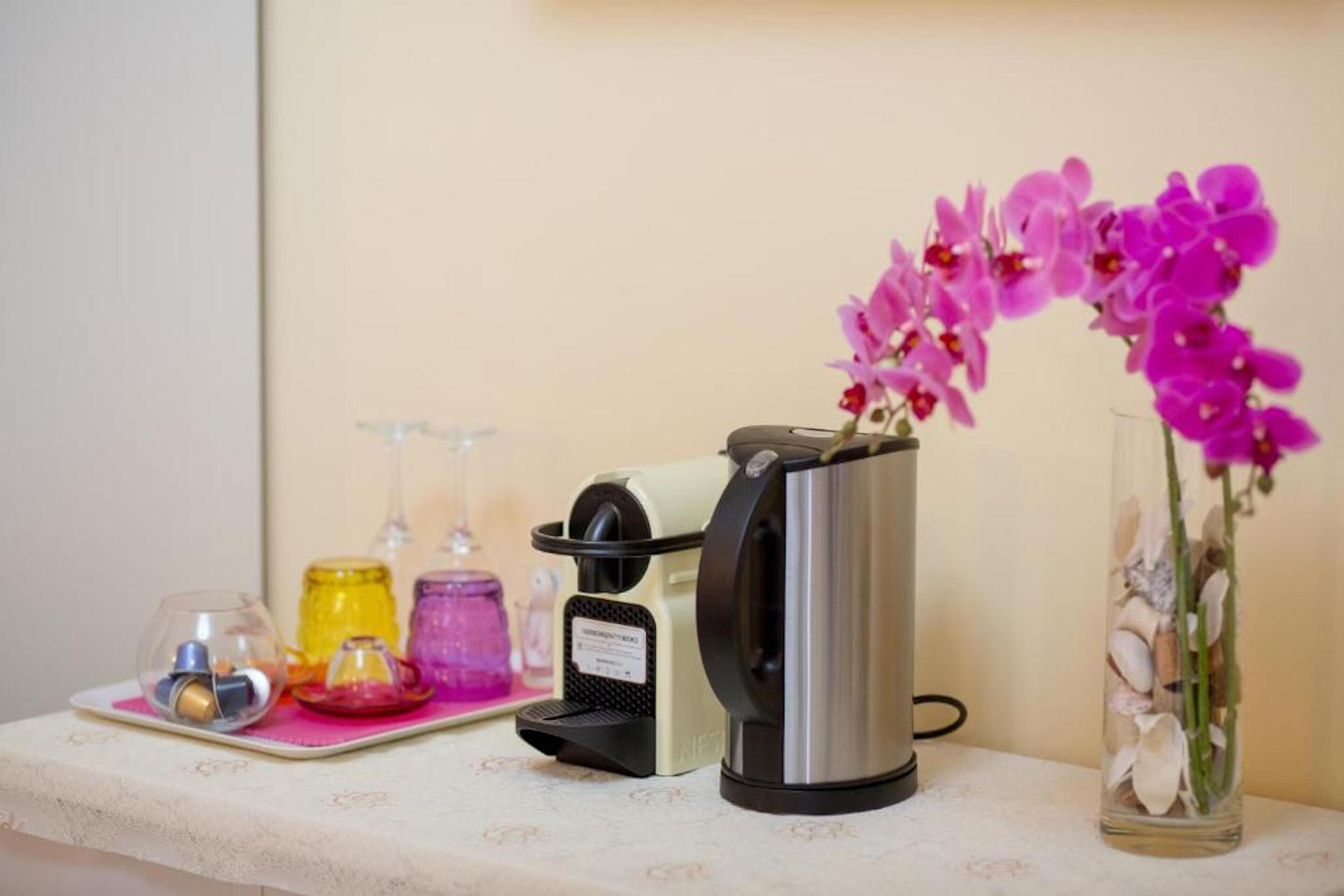 A coffee maker, a glass vase with pink flowers, and various containers on a table.