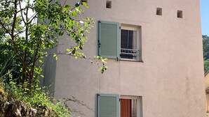 Un edificio con dos ventanas, una con una persiana cerrada y otra con una persiana entreabierta. Cuenta con un pequeño balcón con barandilla metálica.
