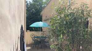 Un pequeño patio al aire libre con una mesa, sillas, una sombrilla azul y una planta en maceta.