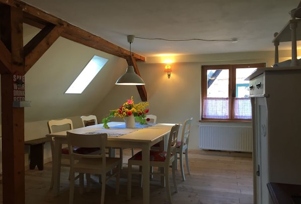 Un coin repas avec une table et des chaises en bois, un vase de fleurs et une lucarne.