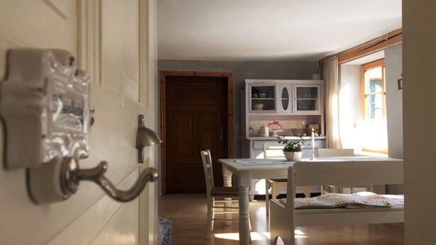 A dining area with a table and chairs, a white cabinet with glass doors, and a wooden door in the background. - Apartment Büdnerei total up to 14 people (Auguste, Heinrich, Ida) (Stuer)