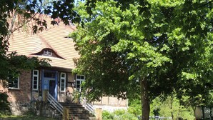A brick building with a red-tiled roof, a staircase leading to the entrance, and a tree in front. - Apartment Büdnerei total up to 14 people (Auguste, Heinrich, Ida) (Stuer)