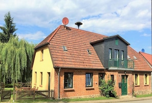 Une maison à deux étages, avec un toit recouvert de tuiles rouges, une antenne parabolique et un petit balcon.