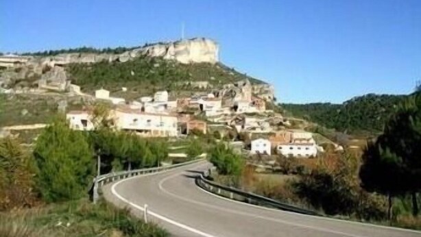 Una carretera serpenteante que conduce a un poblado en la ladera, con construcciones integradas en terreno rocoso.