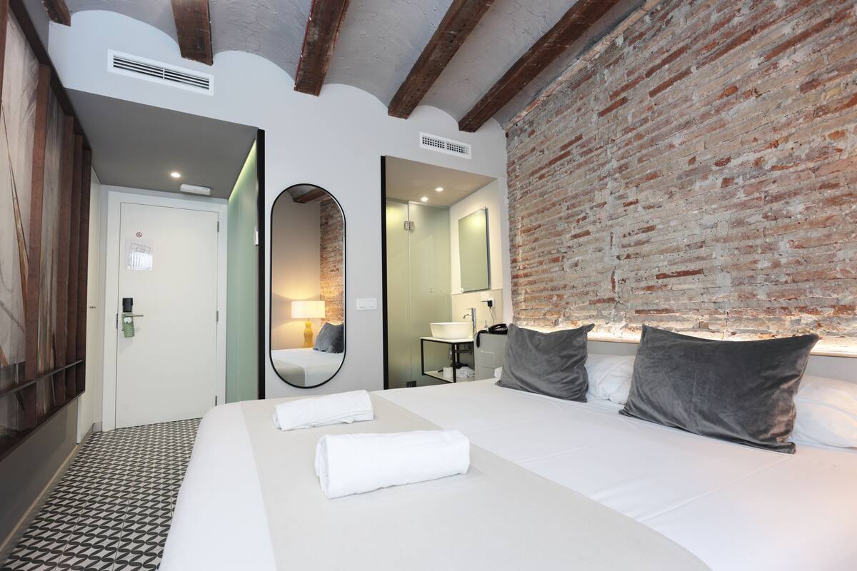 A hotel room with a large bed, a brick wall, a mirror, and a bathroom visible through an open door.