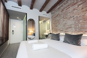 Une chambre d’hôtel avec un grand lit, un mur en briques, un miroir et une salle de bain visible à travers une porte ouverte.