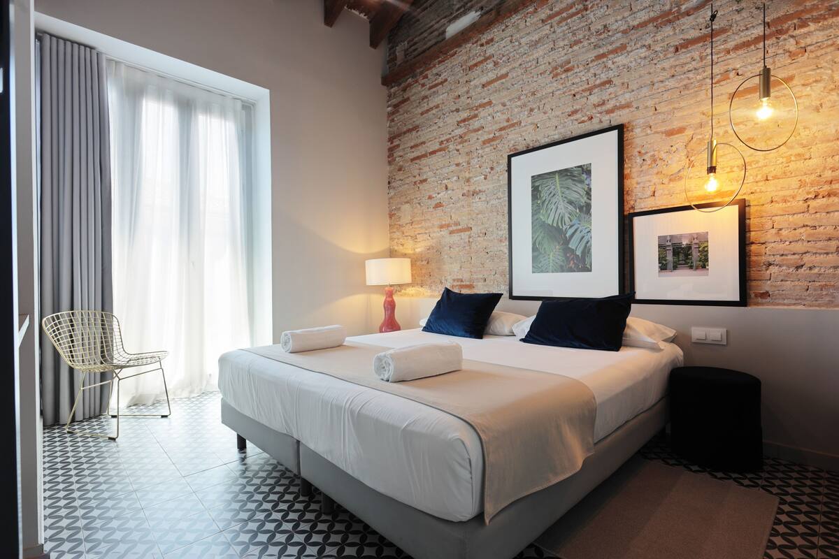 A hotel room with a large bed, a chair, a brick wall, and framed pictures.