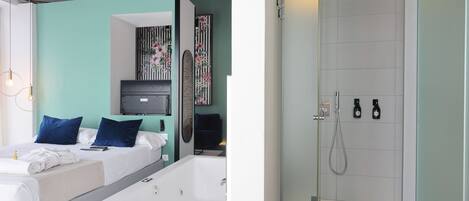 Un dormitorio moderno con una cama grande, una zona de ducha separada y un pequeño rincón de descanso con una mesa y sillas.