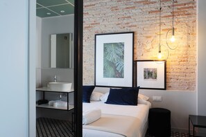 Habitación de hotel moderna con pared de ladrillo, una cama grande, una mesita de noche, un espejo y un cuadro enmarcado en la pared.