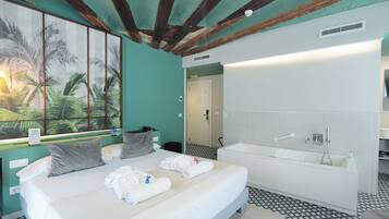 Habitación de hotel con una cama grande, una bañera, un cuadro de palmeras y suelo de baldosas.