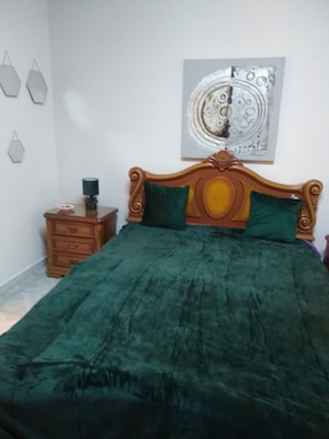 A bedroom with a wooden bed, green pillows, a nightstand, and a wall art piece.