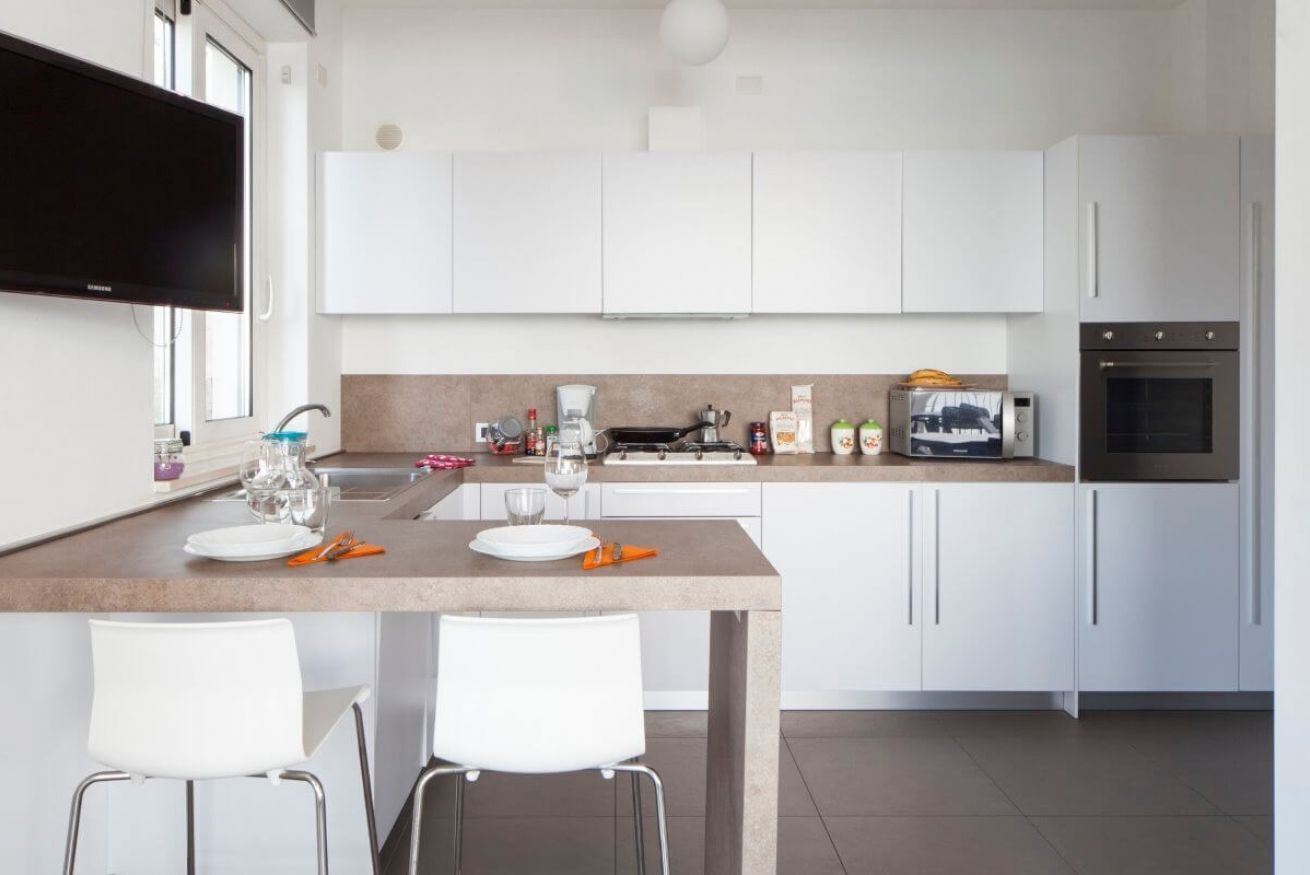 Une cuisine moderne avec des meubles blancs, un téléviseur à écran plat, une machine à café et un four à micro-ondes.