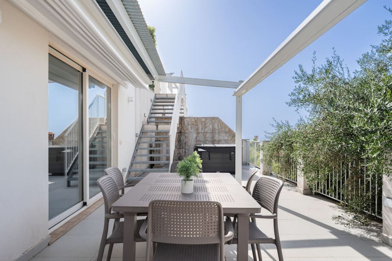 An outdoor patio with a table and chairs, a potted plant, and a staircase leading to a covered area.