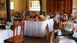 A dining area with multiple tables set for a meal, wooden chairs, and a large window with curtains. - Macheke Lodges & Conference Centre (Macheke)