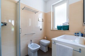 A modern bathroom with a shower, bidet, toilet, and a sink with a towel hanging on the door.