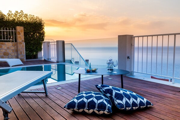 A wooden deck with a pool, lounge chairs, and a table with glasses and a bowl.
