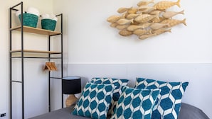 Ein Schlafzimmer mit einem Bett, zwei gemusterten Kissen, einer Wanddekoration mit einem Fisch, einem Regal mit Körben und einem Kleiderständer.