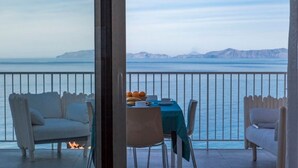 Ein Balkon mit gedecktem Tisch für das Frühstück, mit Blick auf ein ruhiges Meer und ferne Berge.
